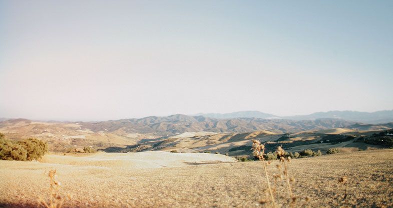 A scenic desert landscape with rolling hills and mountains stretching into the distance under a clear sky.