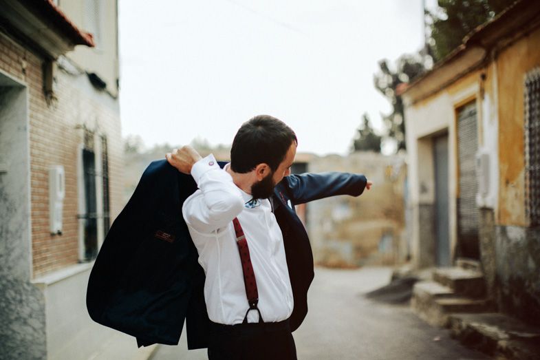 Someone adjusting formal attire while holding a jacket in an alleyway.