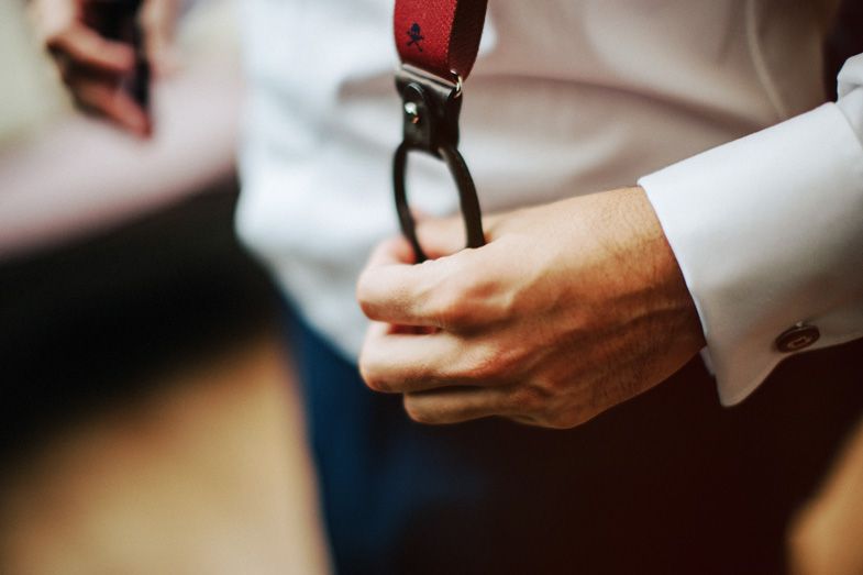 Hands holding red suspender clips during formal dressing preparation.