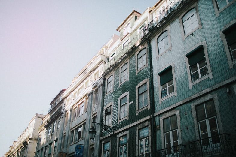 Row of colorful vintage apartment buildings with traditional windows against pastel sky.