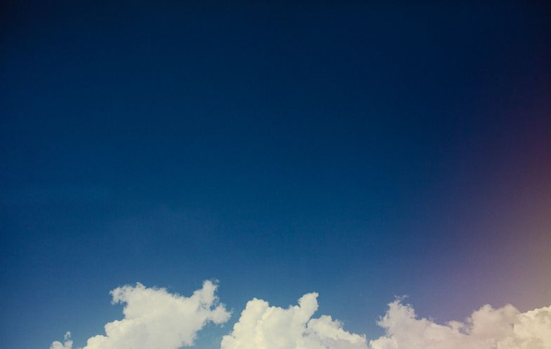 White fluffy clouds against a deep blue sky with a subtle purple gradient.