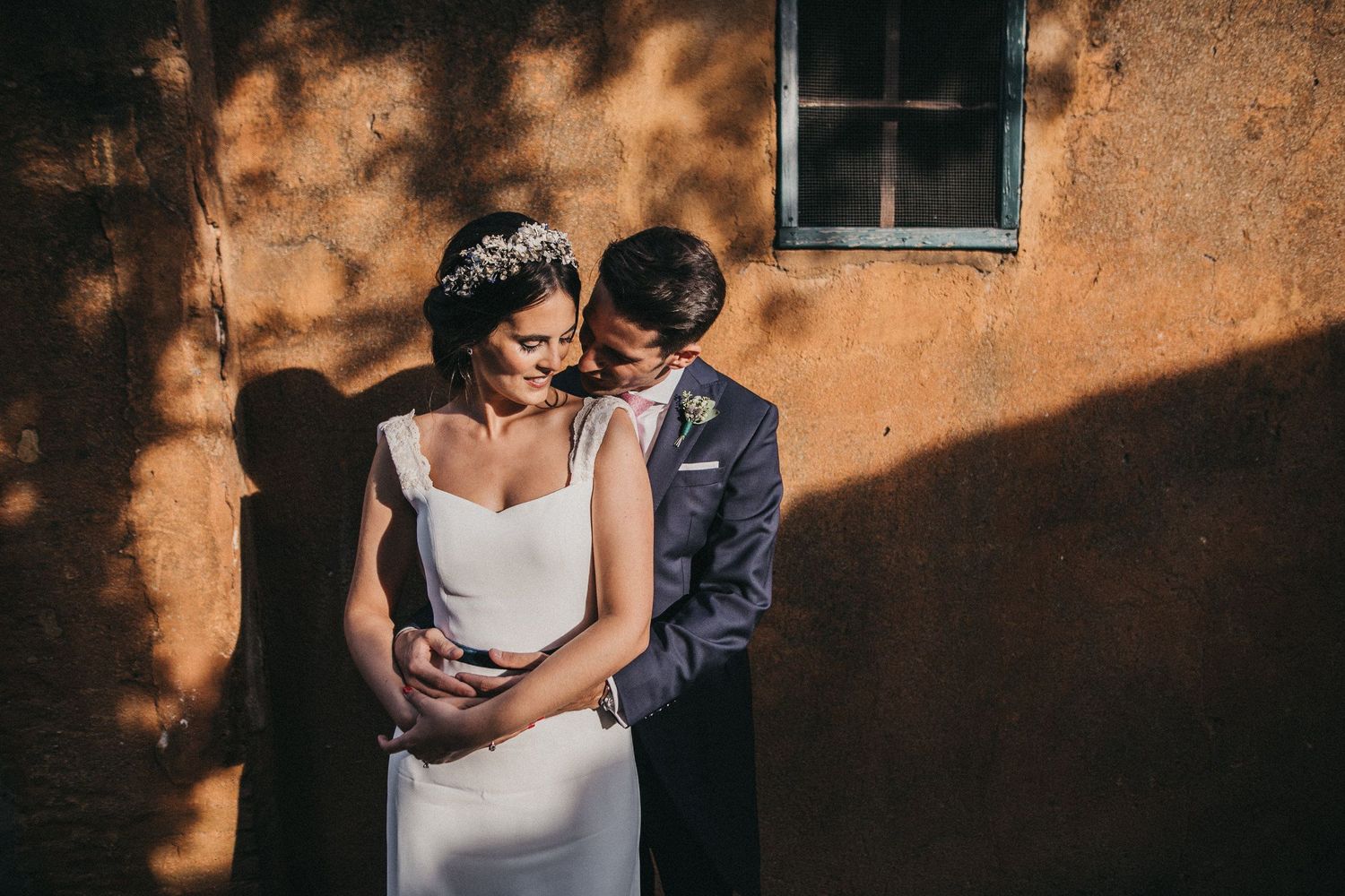 A tender wedding moment captured against a sun-dappled terracotta wall.