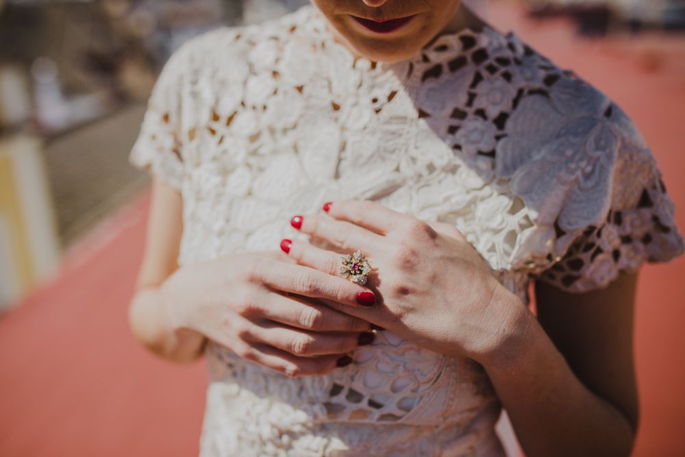 Detailed view of hands with red nail polish and engagement ring against lace dress.
