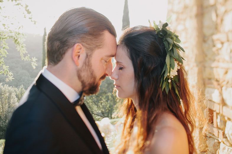 A romantic wedding couple sharing an intimate moment in golden sunlight against a stone wall.