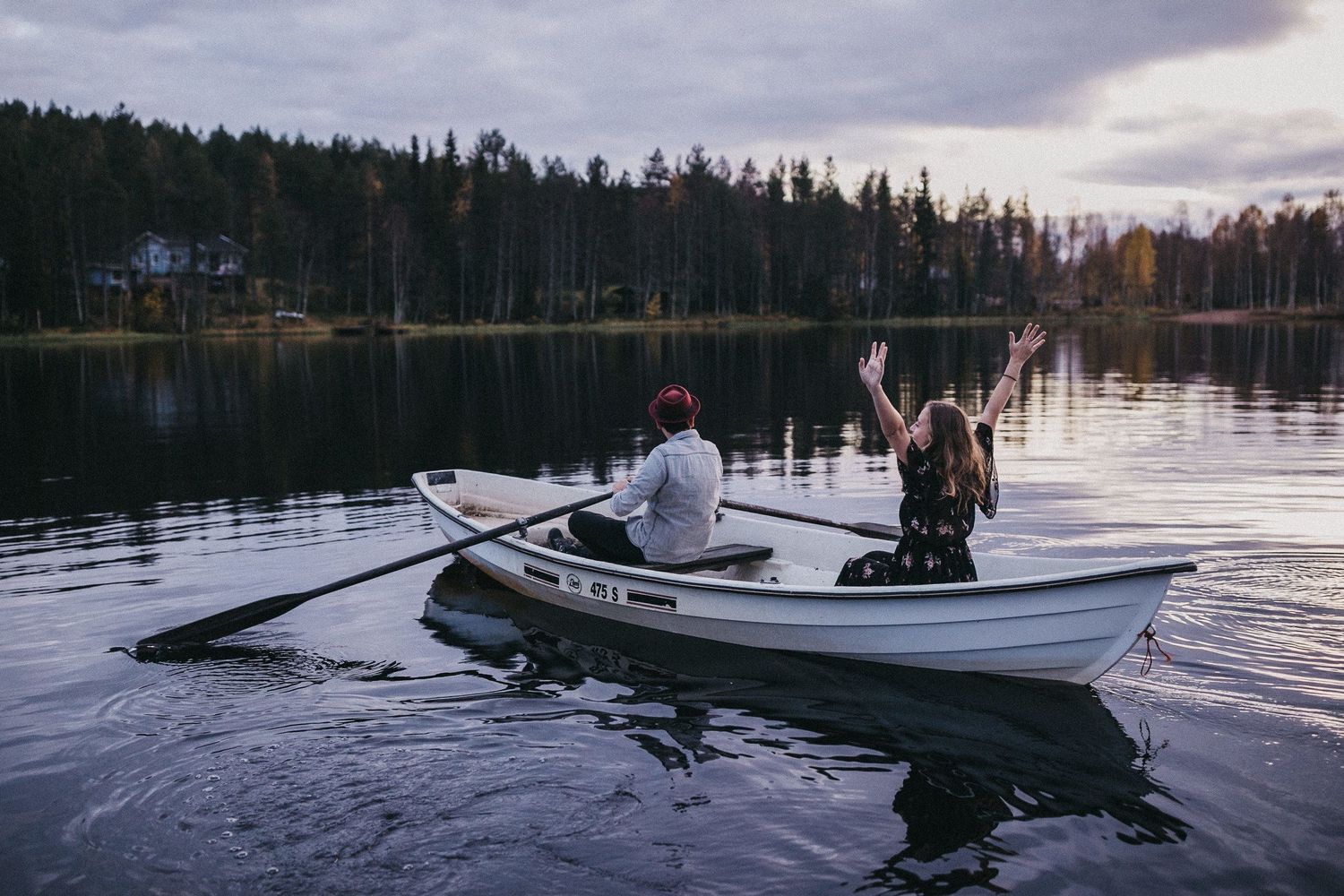A joyful moment captured of a couple in a rowboat on a peaceful lake at sunset.