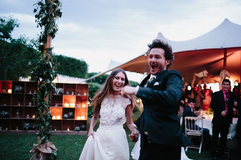 A joyous couple celebrates during their outdoor wedding reception under an orange tent at dusk.