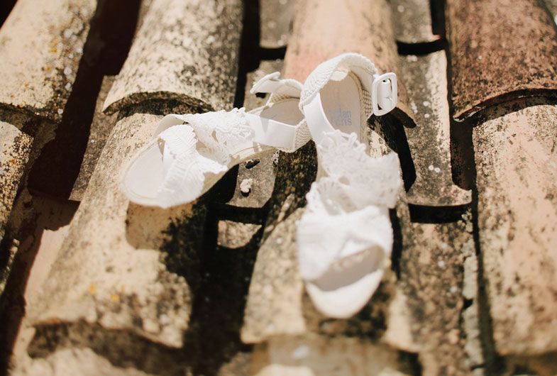 White bridal sandals resting on terracotta roof tiles in natural sunlight.