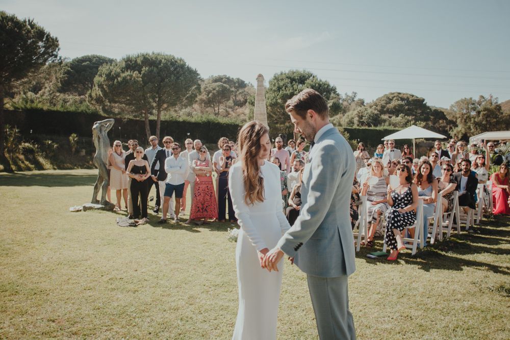 Wedding couple celebrates on sunny lawn surrounded by cheerful wedding guests.