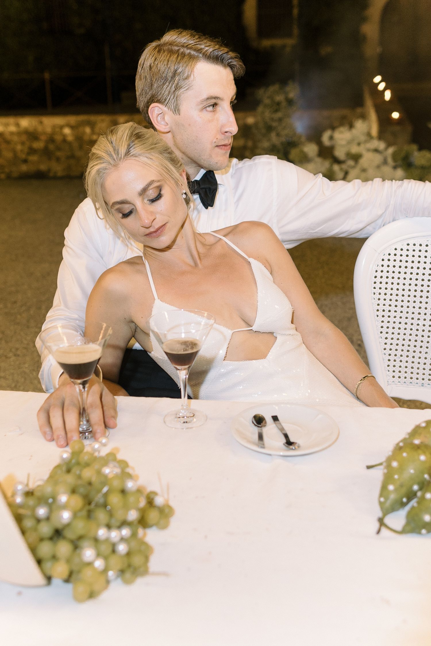 Couple sharing wine and appetizers at an elegant dinner table with white decor and fresh grapes.