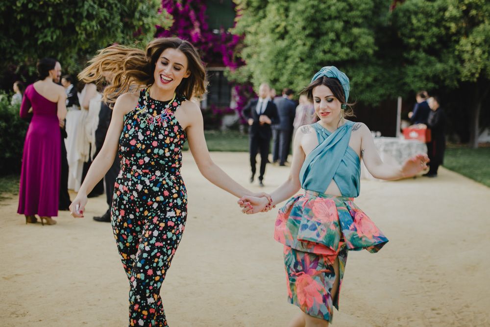 Wedding guests dance and celebrate on a garden path with purple flowers in background.