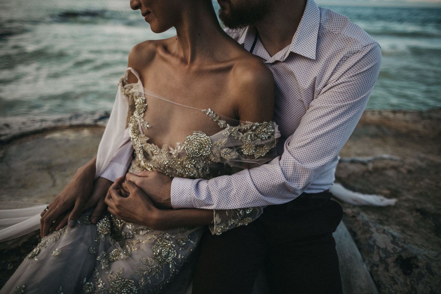An intimate beachside moment captured with lace dress details and ocean waves in the background.
