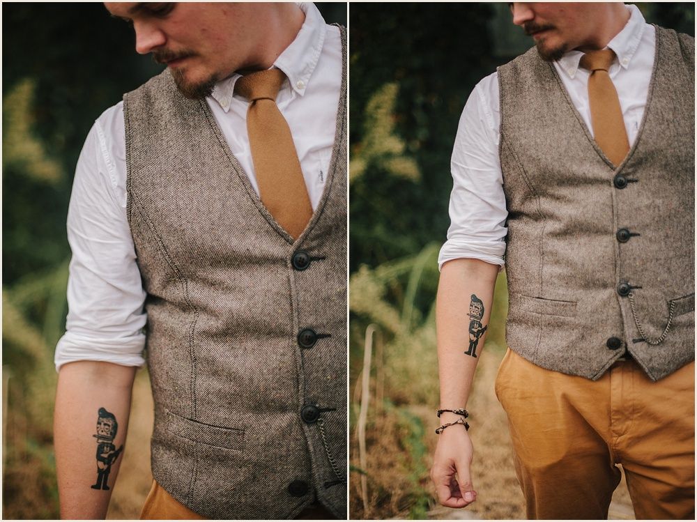 Close-up details of a tweed vest and mustard tie with rolled sleeves showing tattoos.