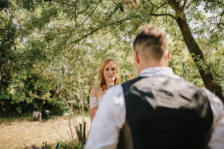 A wedding ceremony takes place in a sun-dappled garden setting with natural decor.