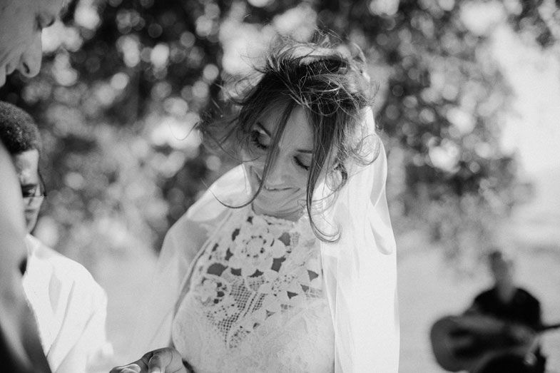 Black and white portrait of a bride in an embroidered dress with a delicate veil at an outdoor wedding ceremony.