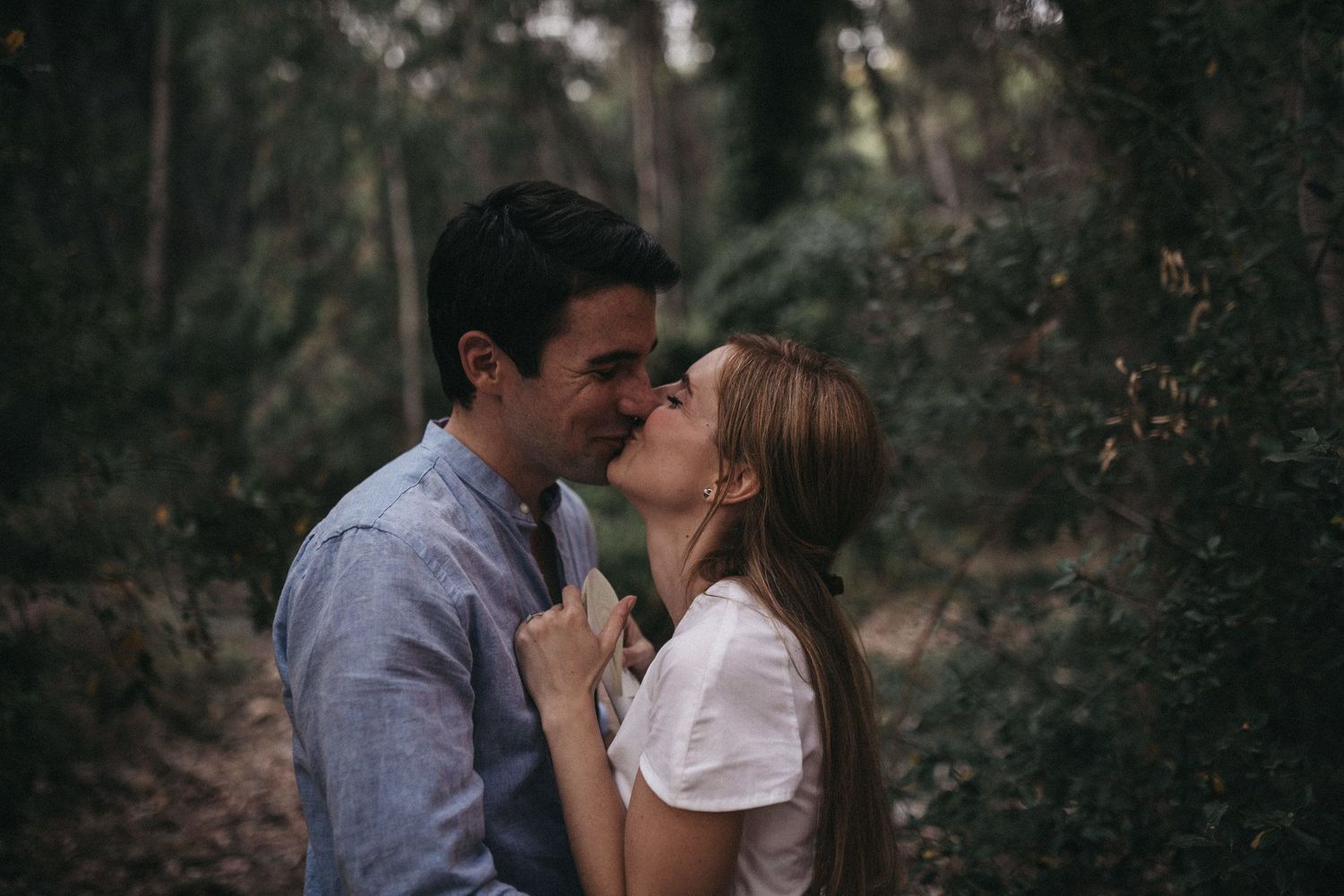 Romantic couple sharing an intimate moment while kissing in a forest setting during an engagement photoshoot.