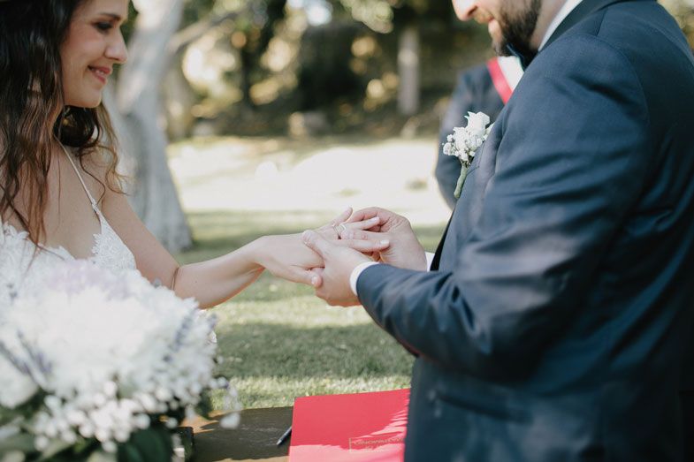 Close-up shot of ring exchange during outdoor wedding ceremony with white flowers.