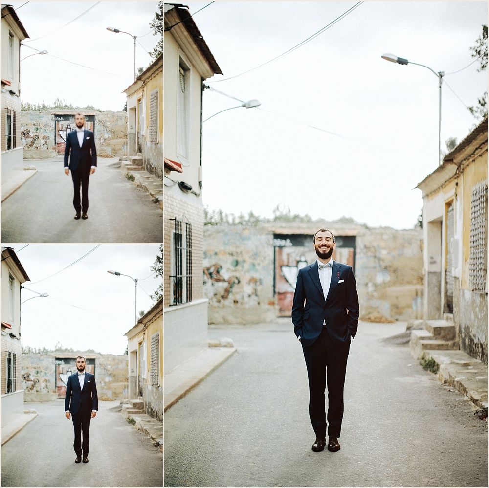 Man in dark suit poses on empty urban street with stone buildings.