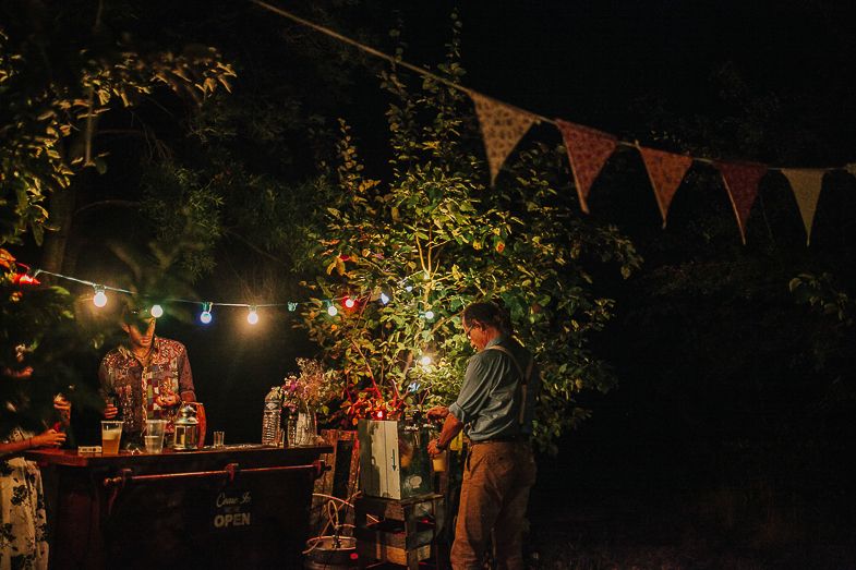 Outdoor nighttime party setting with string lights and red bunting decorations hanging above a rustic bar area.