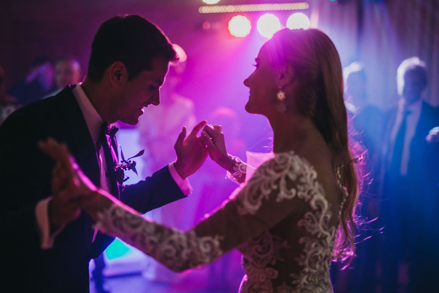 Couple dancing at a wedding reception with purple lighting and romantic atmosphere.