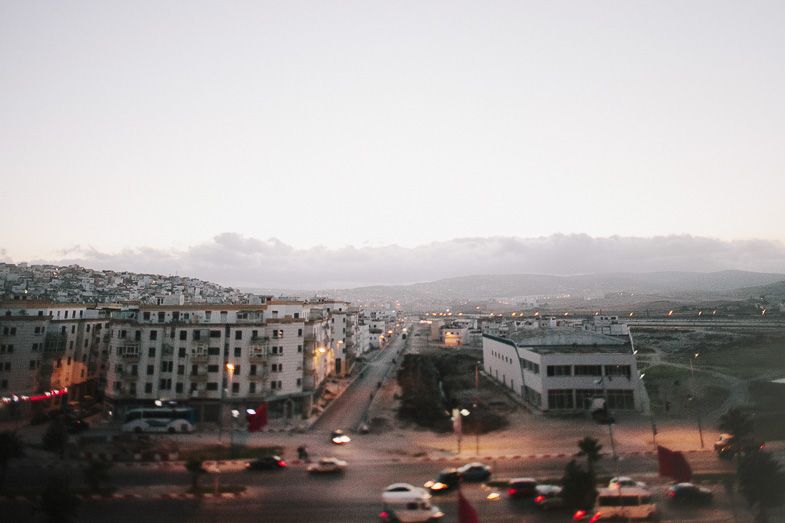 Cityscape at dusk showing apartment buildings and mountains in the distance.