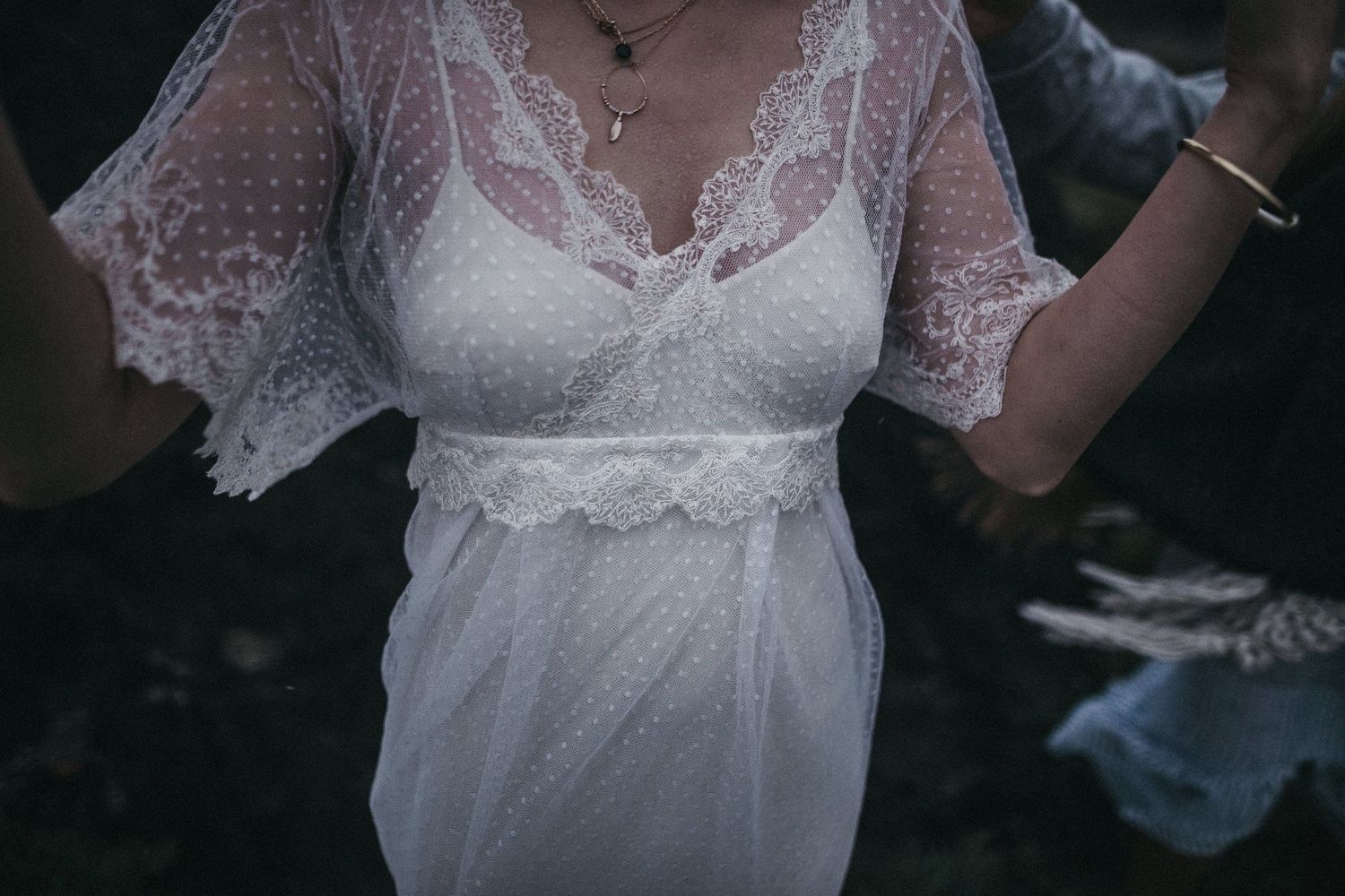 Close-up detail of a delicate white lace wedding dress with flowing sleeves.