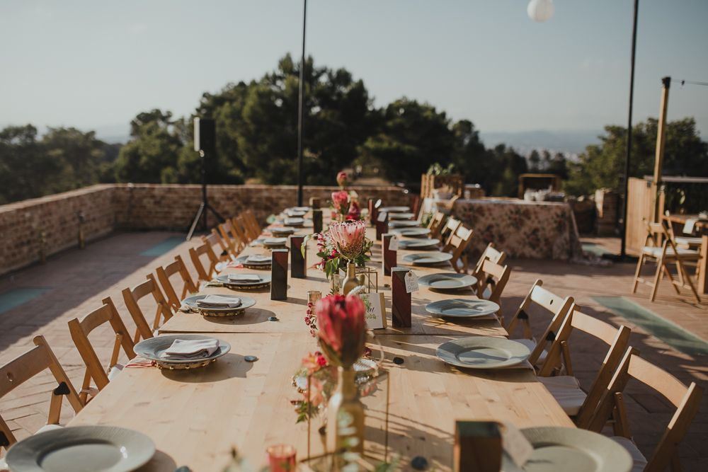 Long outdoor reception table setup with wooden chairs and floral centerpieces.
