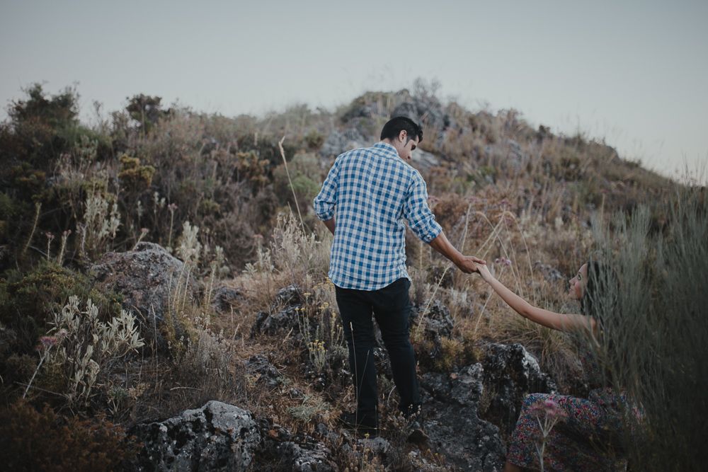 Person in plaid shirt walking along rocky mountain trail in moody lighting.