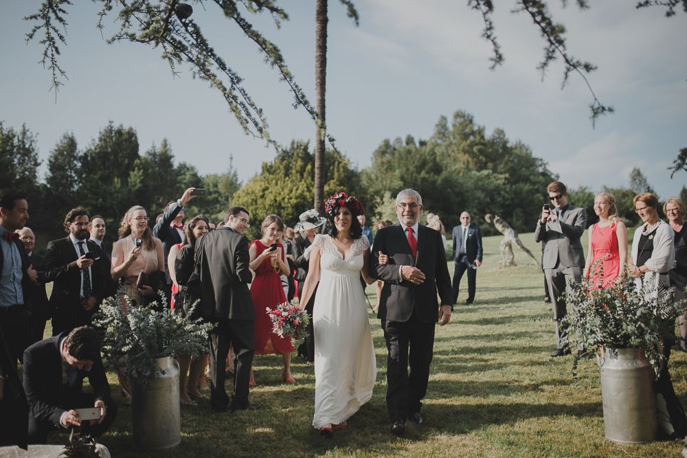 Outdoor wedding ceremony procession with guests lining grassy aisle.