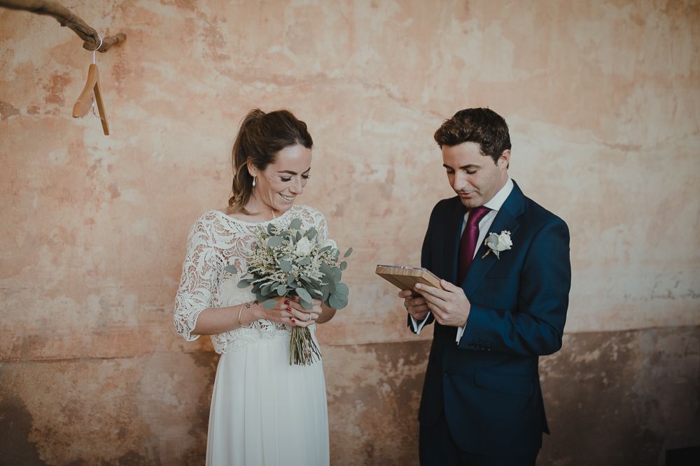 Couple looking at phone while holding wedding bouquet against textured wall.