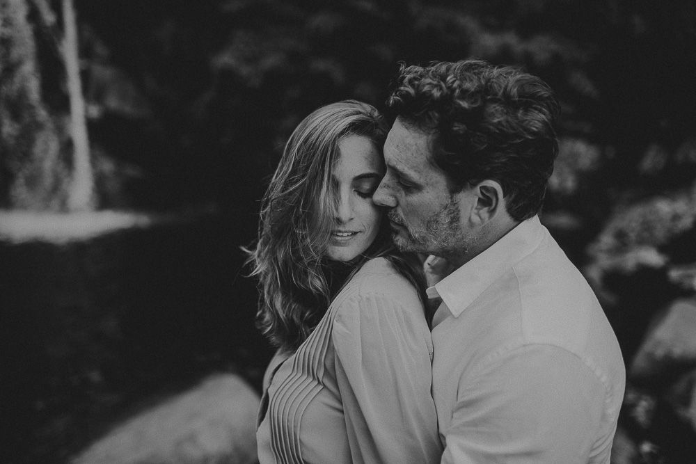 A black and white intimate portrait of a couple sharing a close moment outdoors.