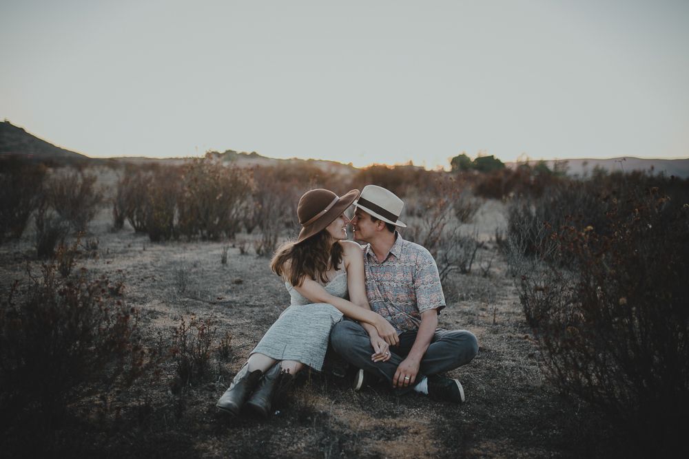 A couple sits together on dry grass during golden hour in a natural outdoor setting.