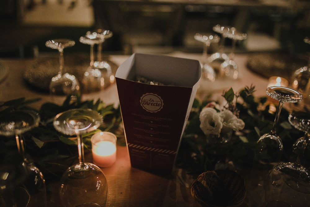 Dark brown menu card sits among glassware and candlelight on an elegant table.