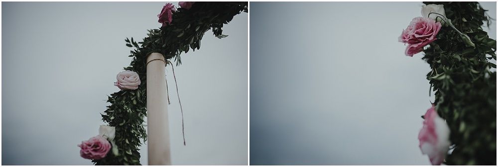 Wedding arch decorated with pink roses and greenery against grey sky.