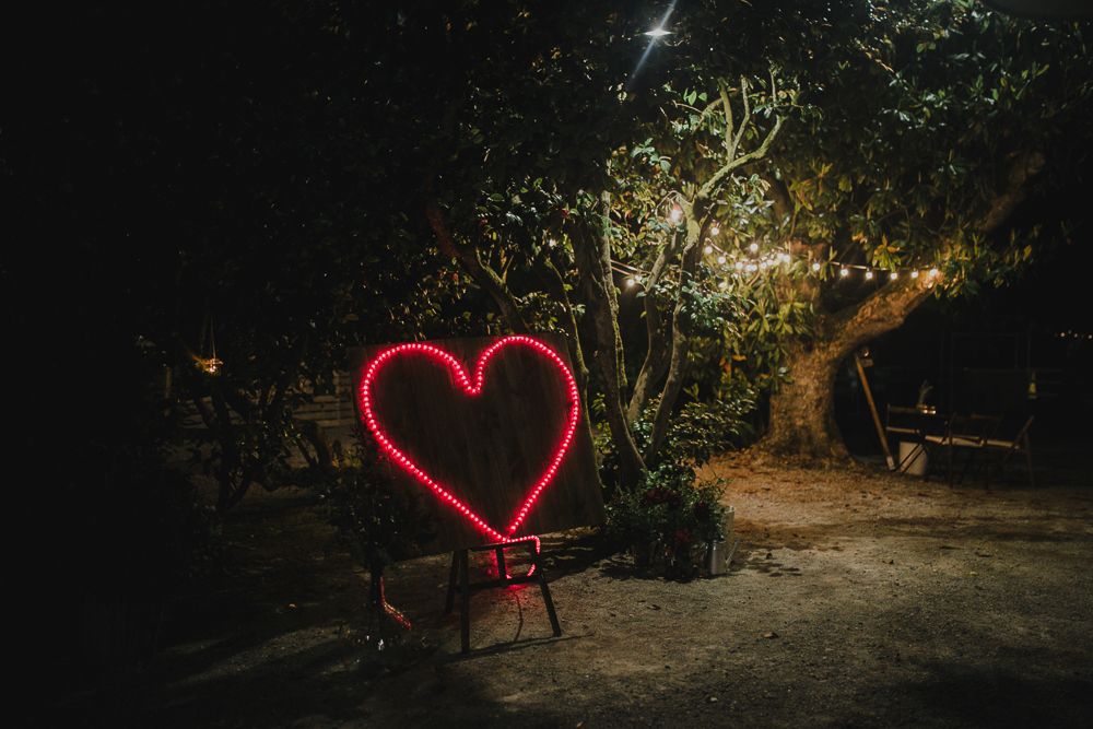 Glowing neon heart light installation illuminates garden path at night.