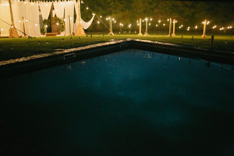 A swimming pool illuminated by string lights at night during an outdoor event.