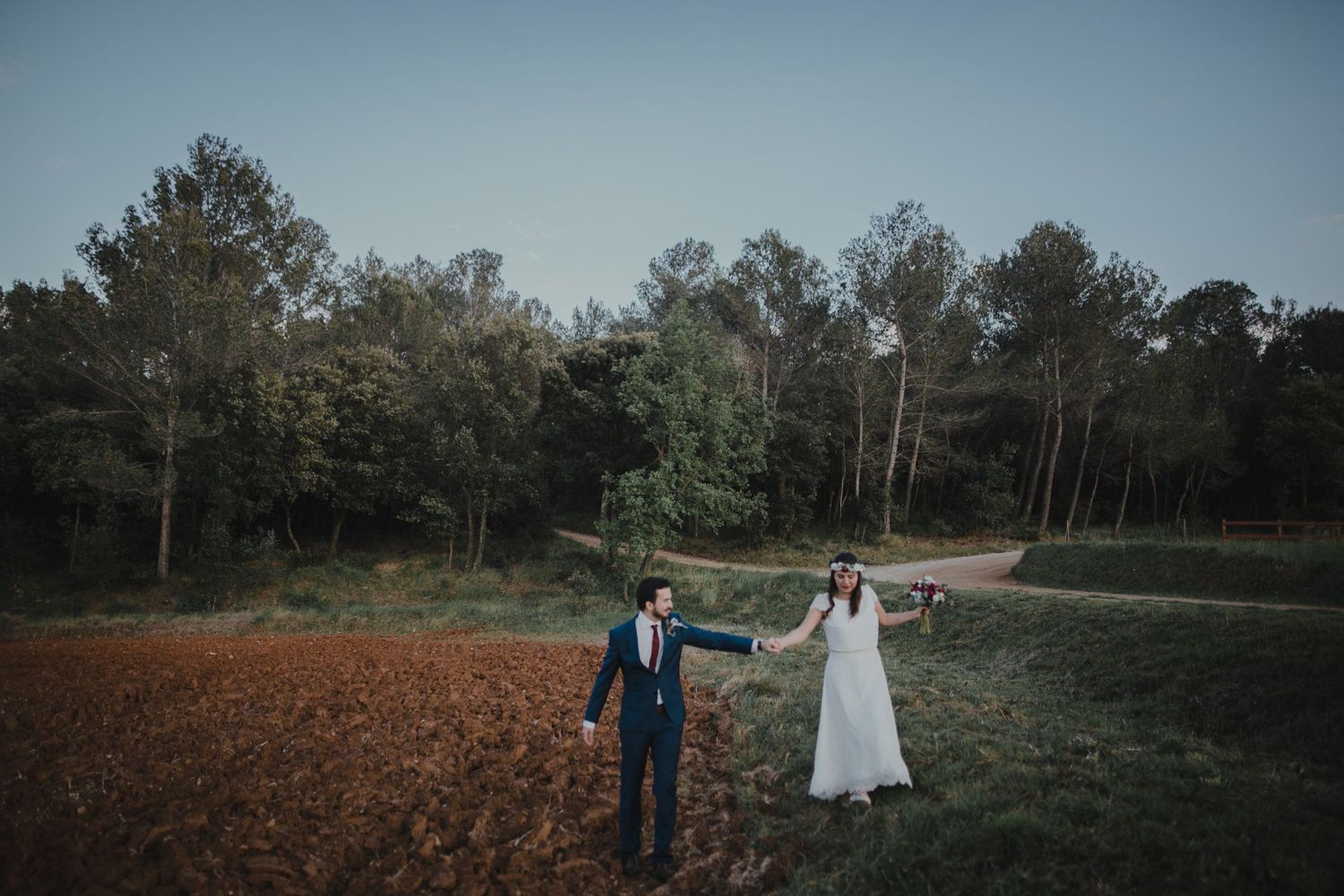 A newlywed couple poses in an open field with trees in the background during golden hour.
