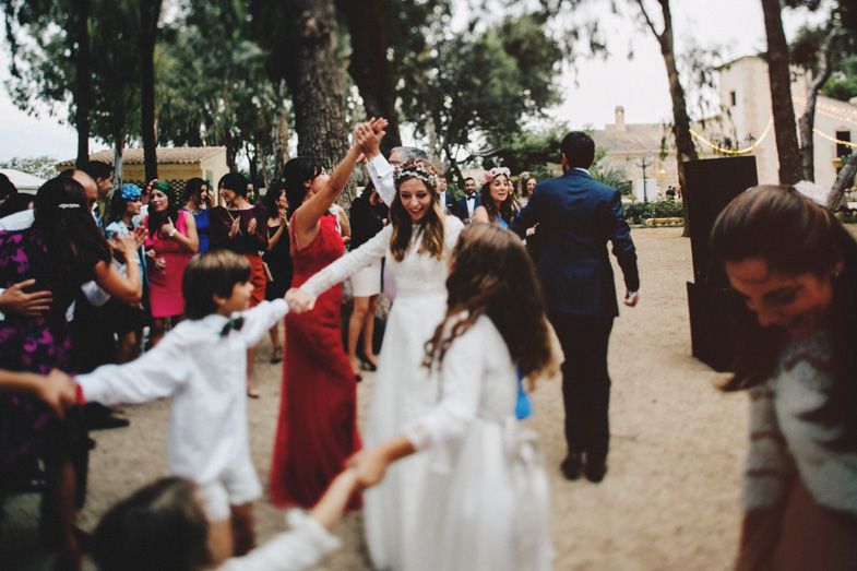 A joyful wedding celebration with guests gathered on a tree-lined path outdoors.
