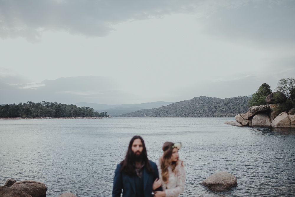 A couple and their dog enjoy a peaceful moment on rocky shores of a mountain lake.