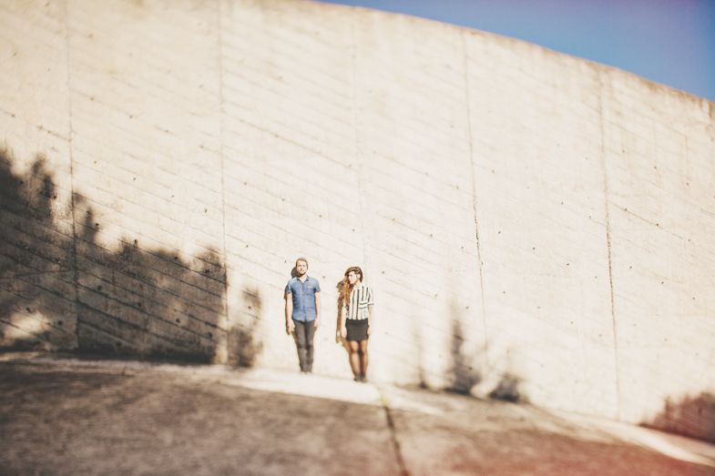 Blurred silhouettes of two people walking along white wall under blue sky.