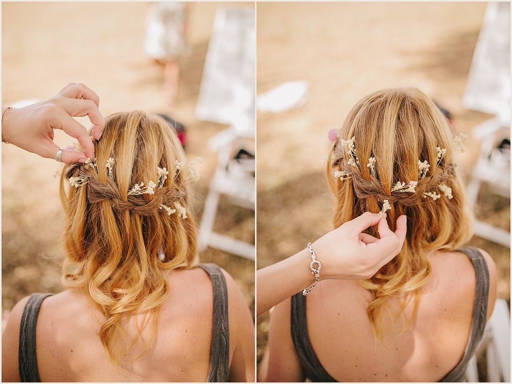 Intricate waterfall braid hairstyle being styled with small flowers woven throughout.