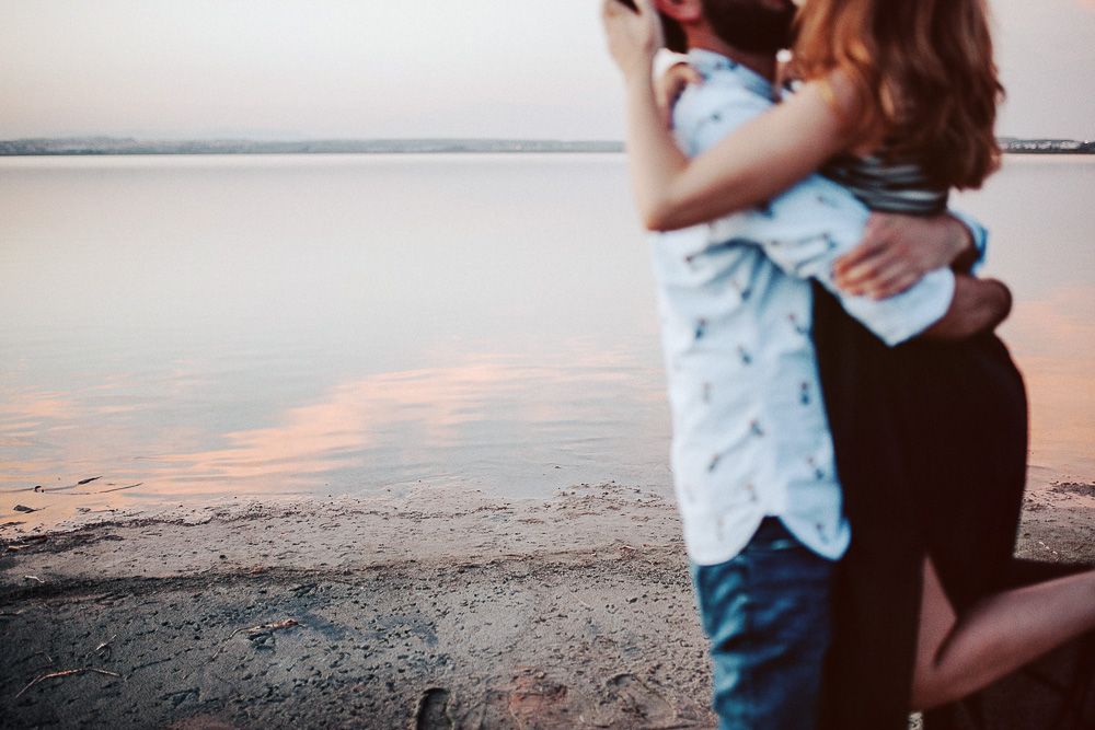 A couple embraces on a beach during sunset.