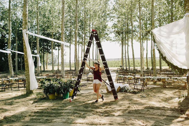 Event setup in progress with ladder and fabric draping between forest trees.