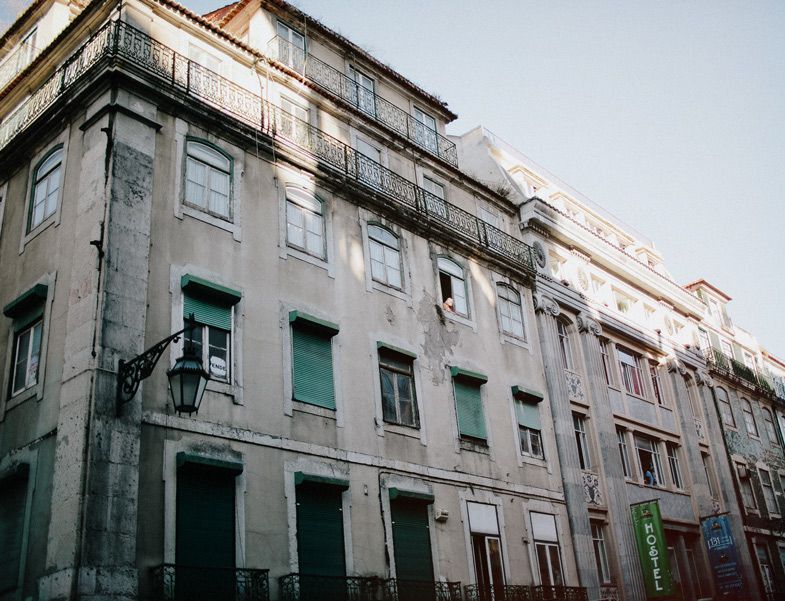 Worn apartment building facade with green shutters and multiple balconies in Lisbon.