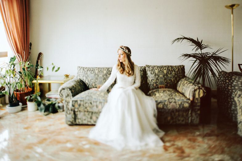 A wedding dress flowing elegantly against a floral sofa and indoor palm plants.