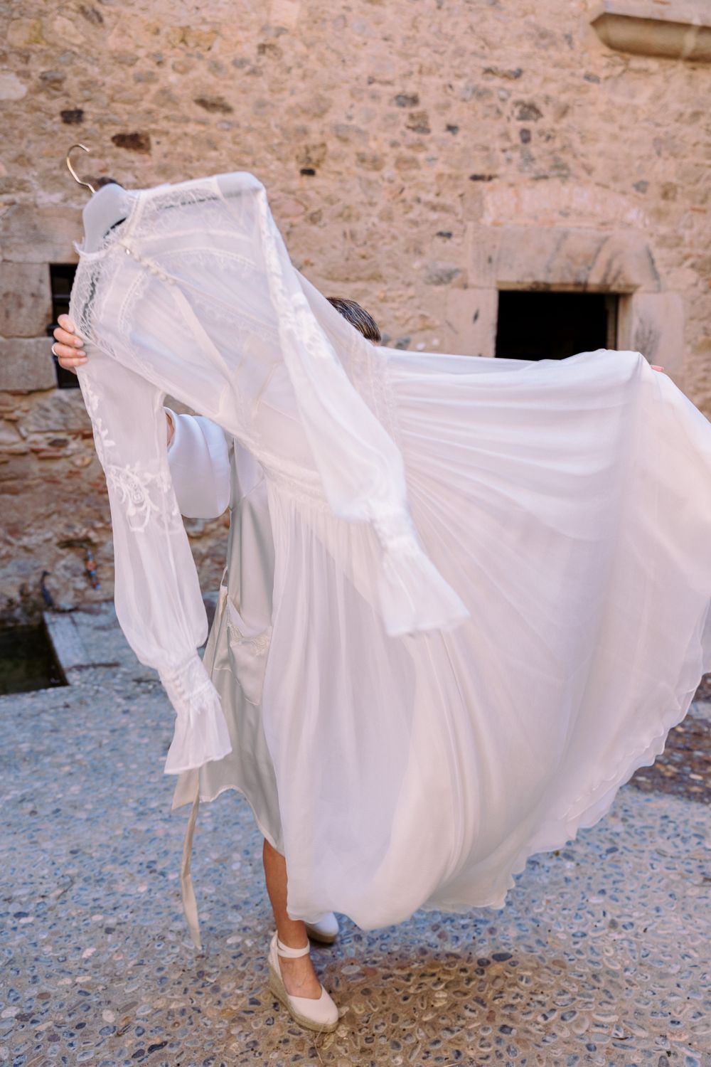 Flowing white wedding dress skirt and heels against a stone wall background.
