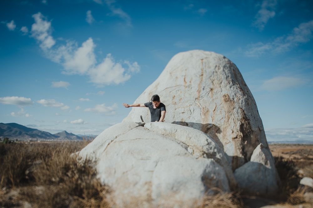 Person sits on large white boulder formation in desert landscape under blue sky.