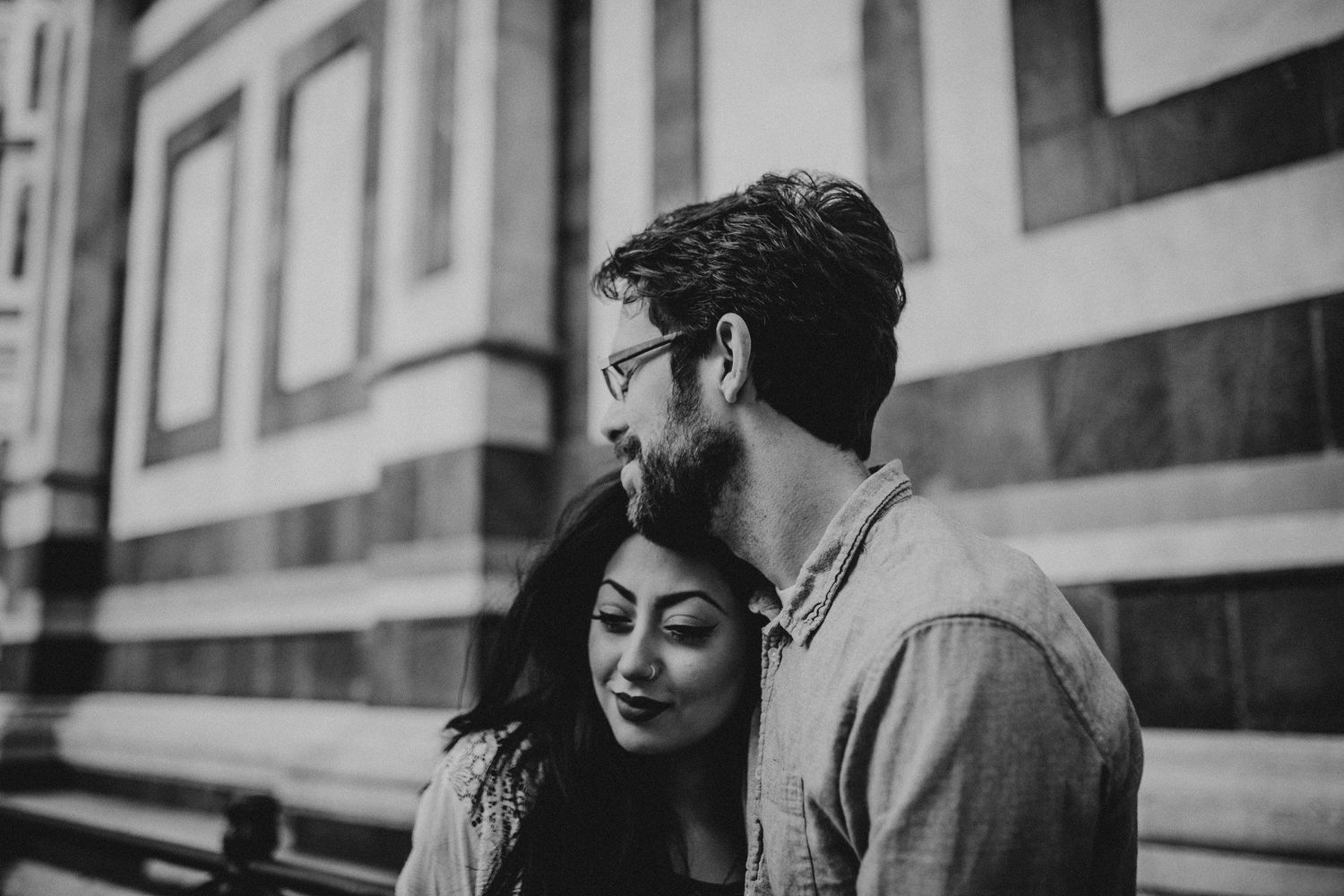 Black and white photo of tender moment between couple against cathedral wall.