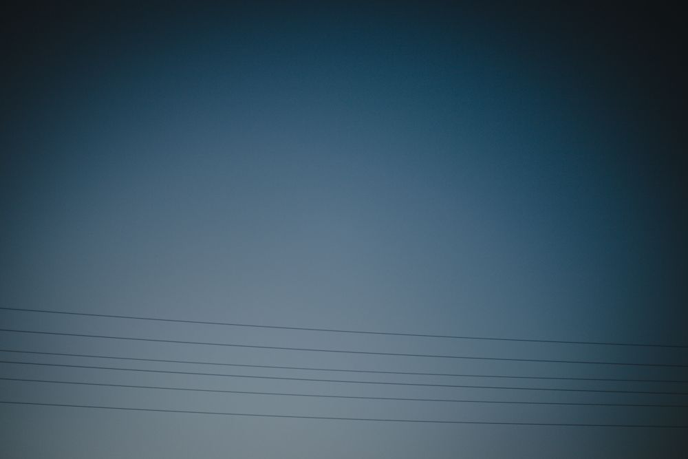Power lines silhouetted against a dark blue gradient sky at dusk.