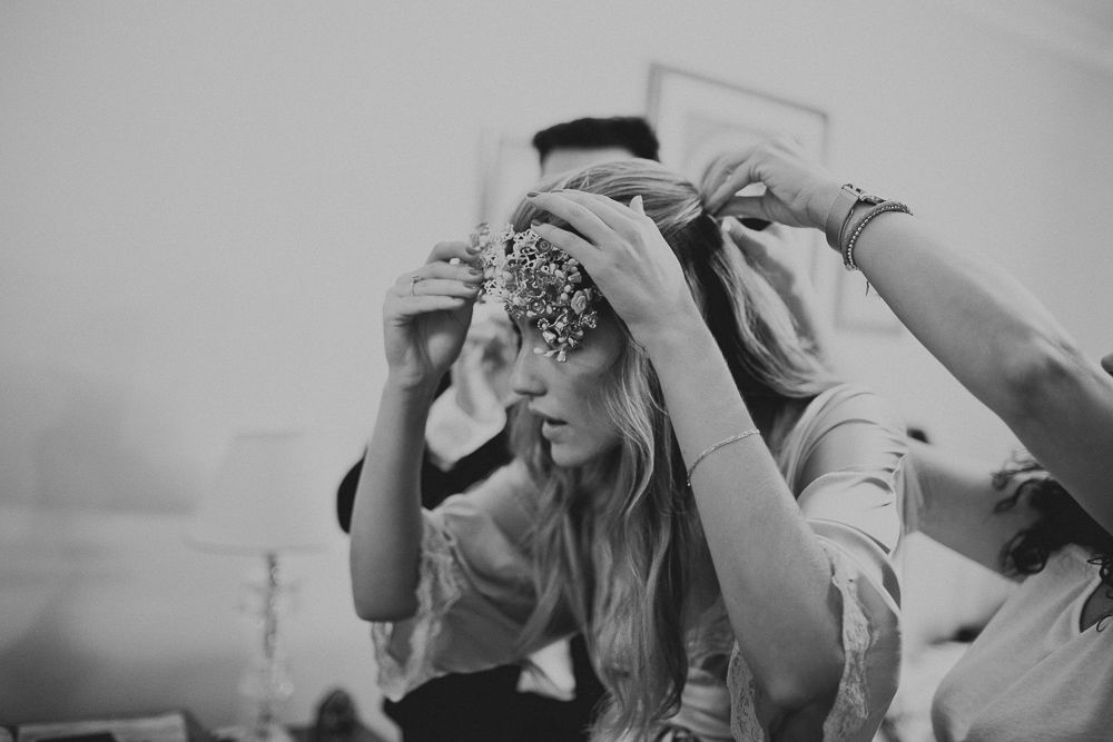 A black and white wedding photo showing preparation with an ornate headpiece being placed.