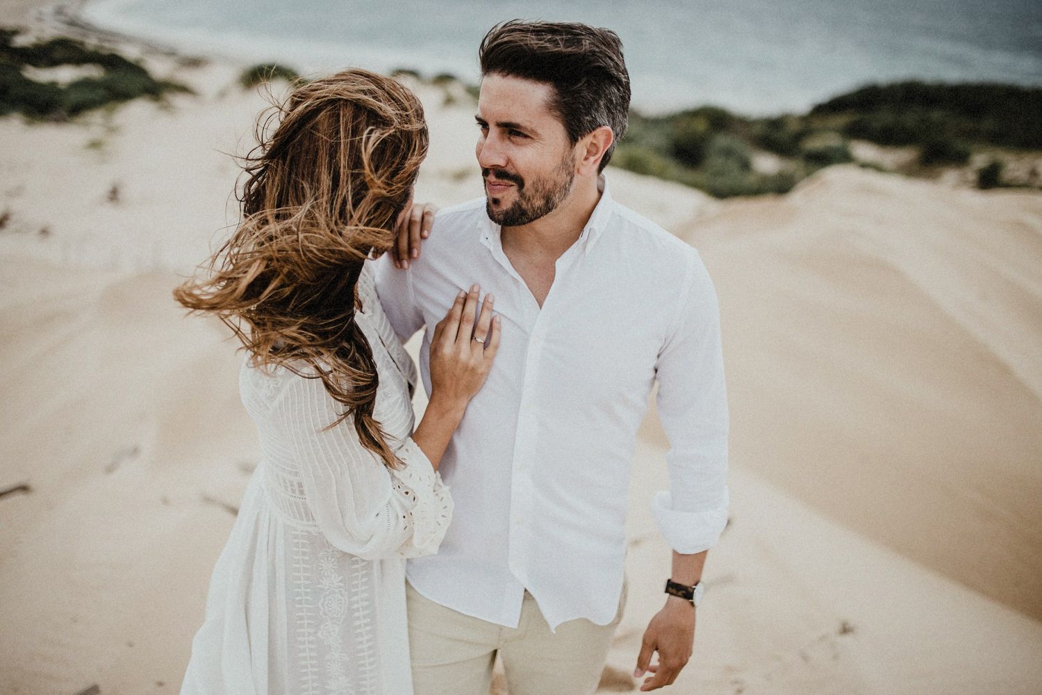 Dreamy coastal photoshoot of couple in white attire on sand dunes.
